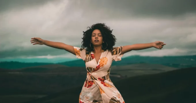 a black woman standing in a powerful pose with arms wide and mountains behind her