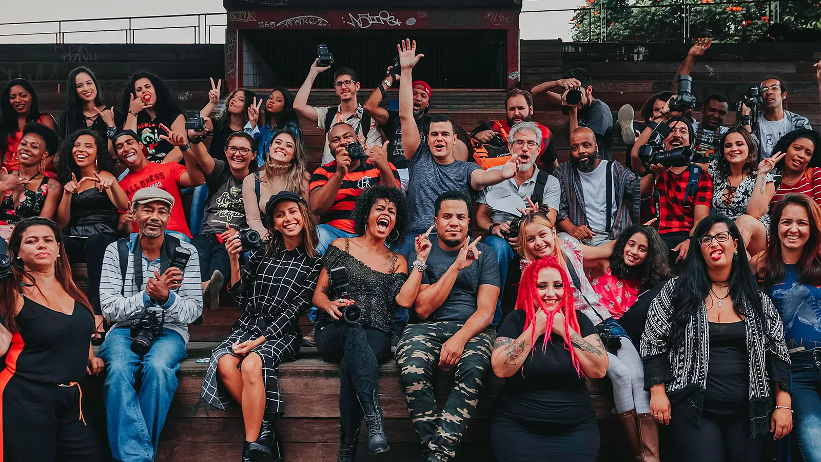 a group of 60 racially diverse people smiling at the camera with their arms raised