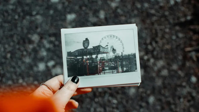 a white woman's hand holding a faded polaroid photo of an amusement park