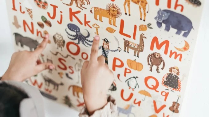 a closeup of a poster with the alphabet on it and a white girl pointing to letters