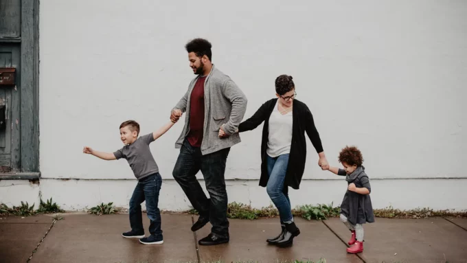 a mixed-race family of four, a male and female parent and two children walking on a sidewalk