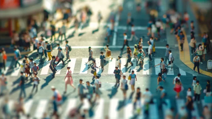 a tilt-shift effect of toy-like people crossing a street at a busy city crosswalk