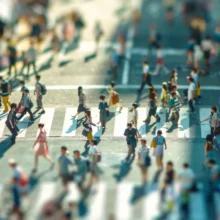 a tilt-shift effect of toy-like people crossing a street at a busy city crosswalk