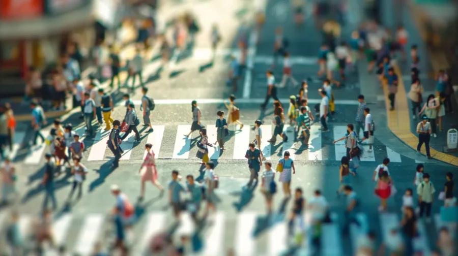 a tilt-shift effect of toy-like people crossing a street at a busy city crosswalk