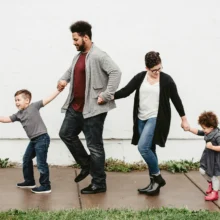 a mixed-race family of four, a male and female parent and two children walking on a sidewalk