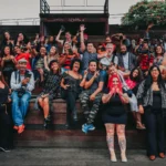 a group of 60 racially diverse people smiling at the camera with their arms raised