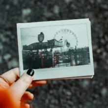 a white woman's hand holding a faded polaroid photo of an amusement park