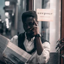 a black man sitting at an outdoor cafe reading a newspaper