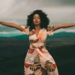 a black woman standing in a powerful pose with arms wide and mountains behind her