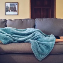 a white man lying on couch with blanket over head sick
