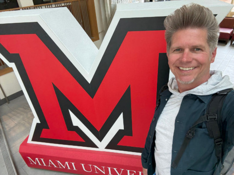 dennis cheatham portrait standing next to a miami university M logo statue in a visitor center building
