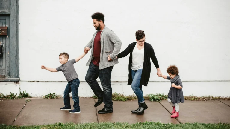 a mixed-race family of four, a male and female parent and two children walking on a sidewalk