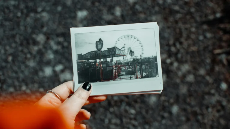 a white woman's hand holding a faded polaroid photo of an amusement park